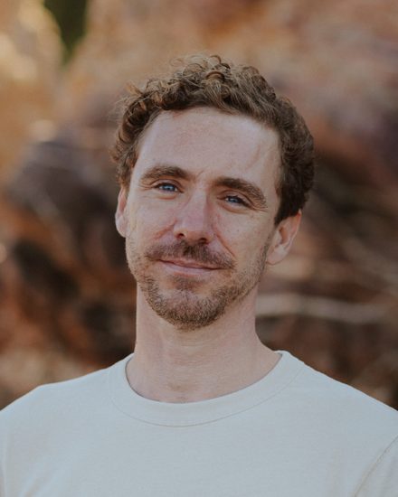 Joe Collings, standing outdoors in front of weathered orange rock.